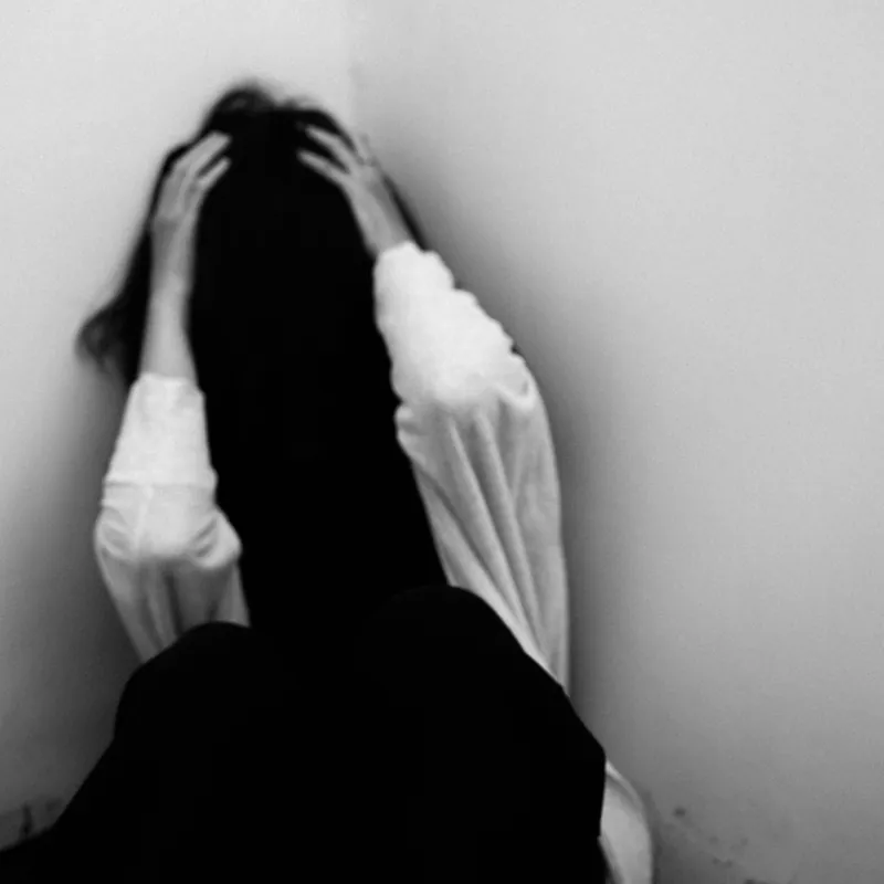 Mujer sentada en un rincón con las manos en la cabeza, desbordada por la ira