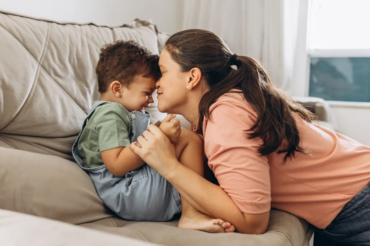Madre y su hijo riendo frente con frente en el sofá, educar sin gritar con calma y cariño