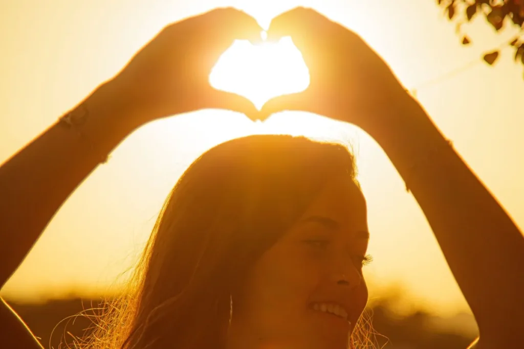 Mujer sonriendo al atardecer con las manos en forma de corazón tras aprender a controlar la ira