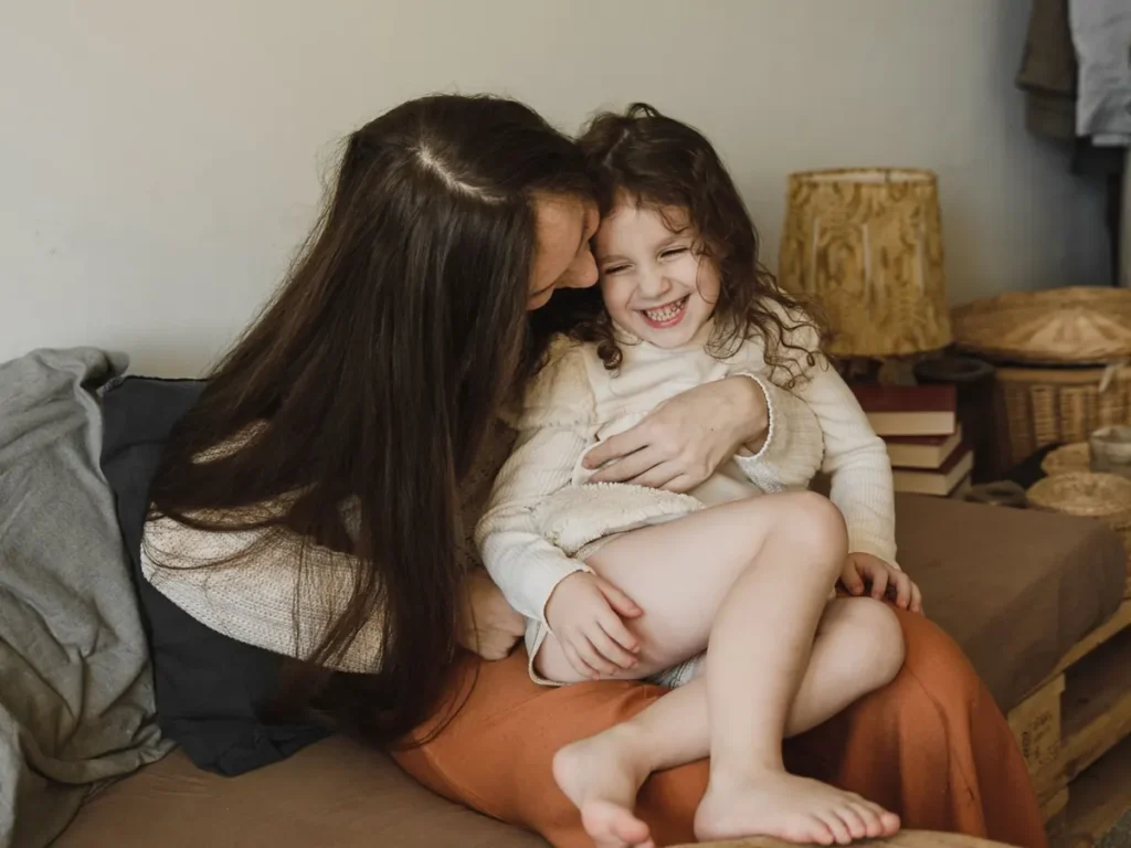 Madre e hija riendo juntas en el sofá, curso para hablar con tus hijos