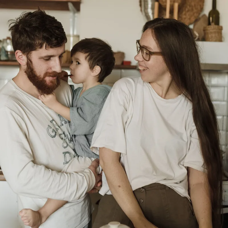 Padre con su hijo en brazos y madre sonriendo en la cocina por la mañana