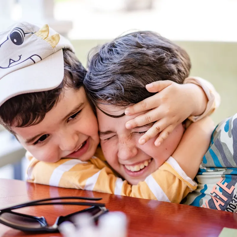 Dos hermanos abrazados y riendo juntos en la mesa