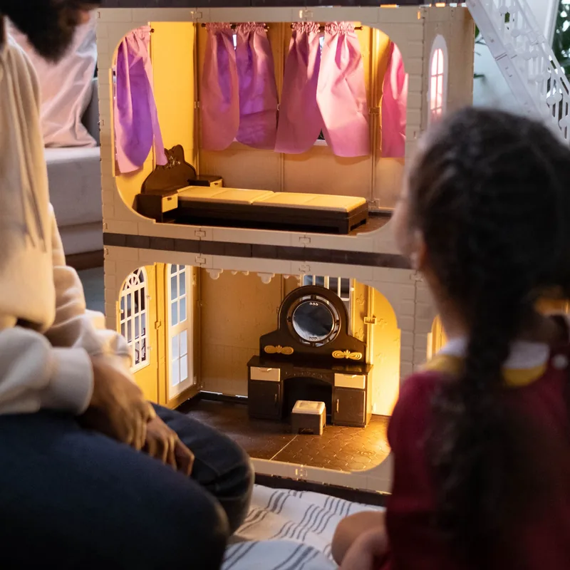 Padre e hija jugando juntos con una casa de muñecas en el salón